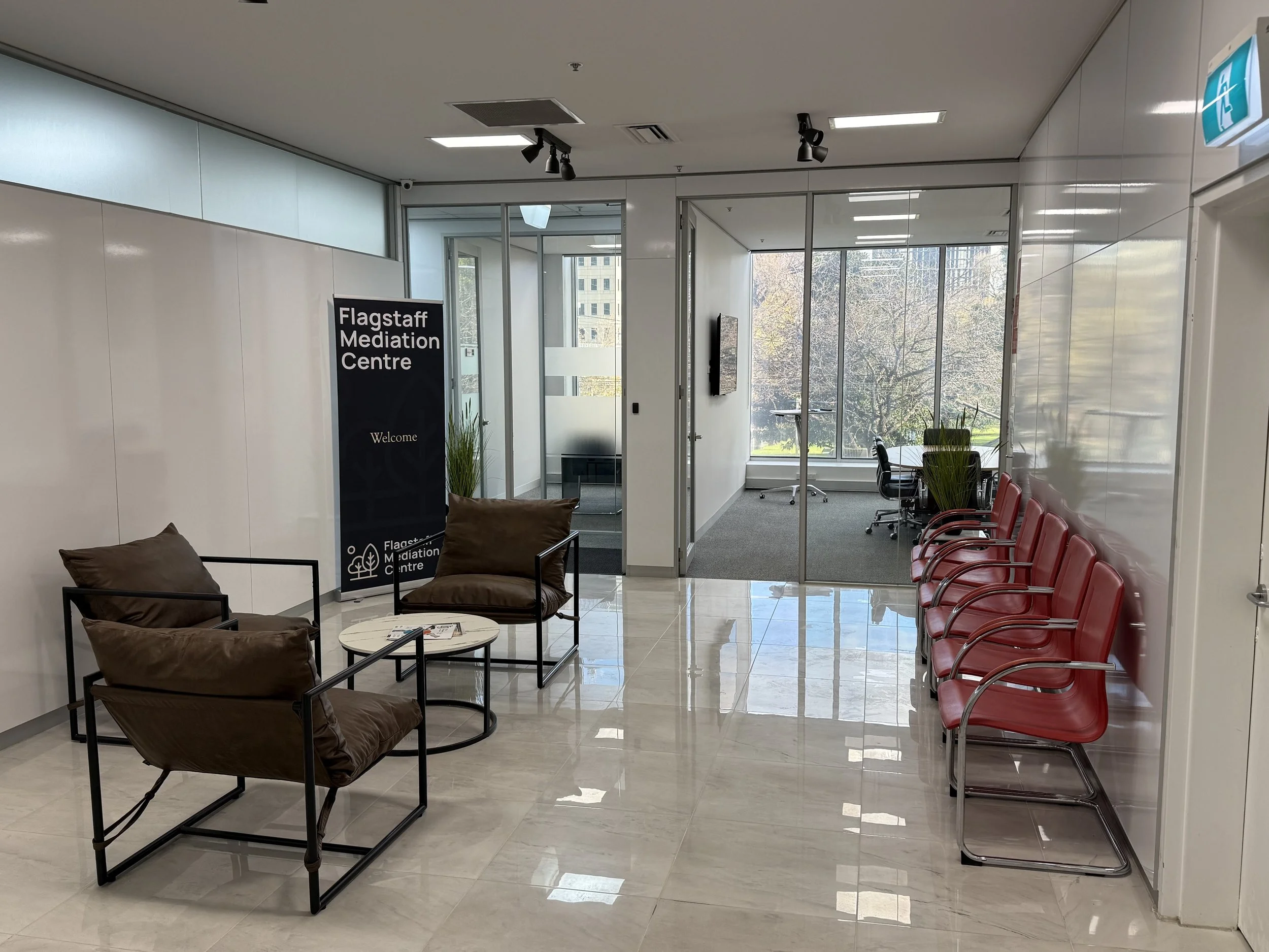 Interior of the Flagstaff Mediation Centre with chairs and consultation areas, large windows with a view of trees outside, and a sign welcoming visitors.