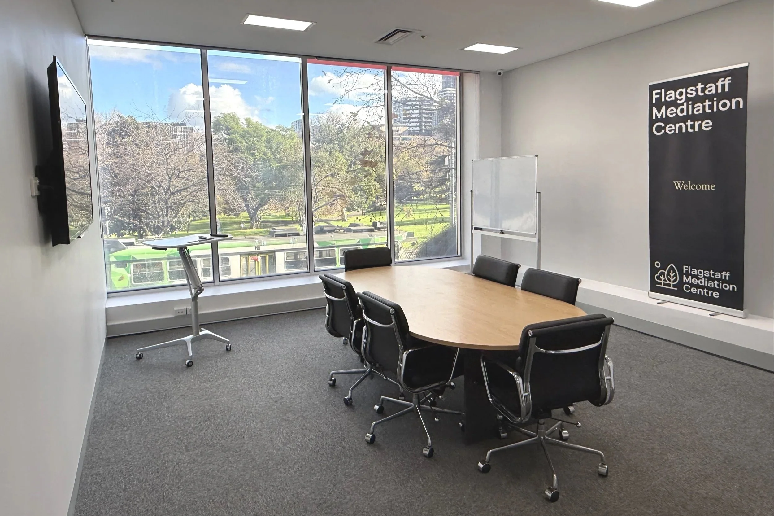 Flagstaff Mediation Centre joint session Flagstaff Mediation Room 1 overlooking Flagstaff Gardens and featuring a conference table, wall-mounted LED screen, wheeled 2-sided whiteboard.
