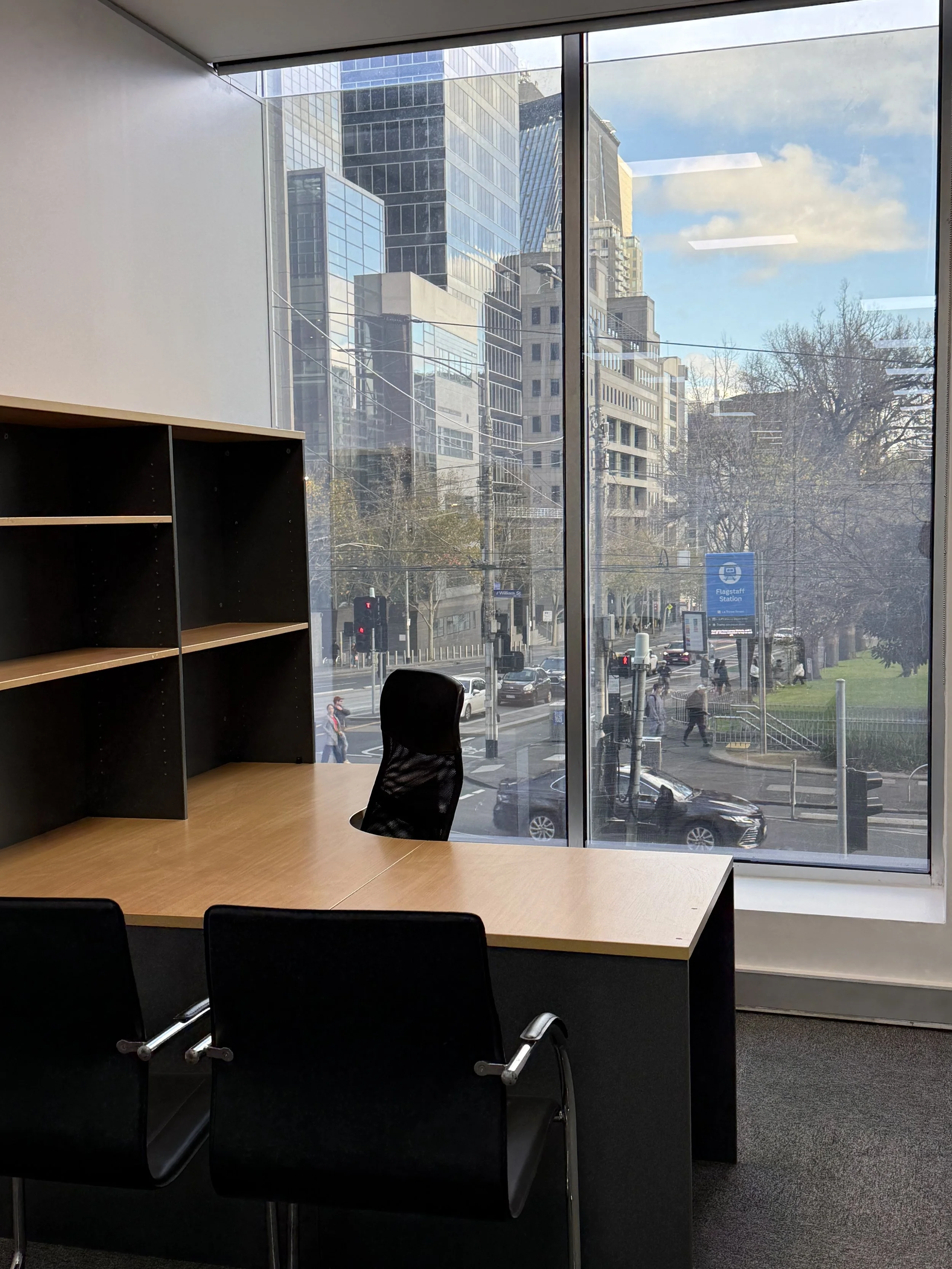 Flagstaff Mediation Centre - typical breakout room layout - an office with a light wooden table, black chairs, and large window showing city buildings, street, and people outside.