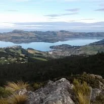 A scenic view of a lake with surrounding hills and a small town in the distance, seen from a mountain trail.