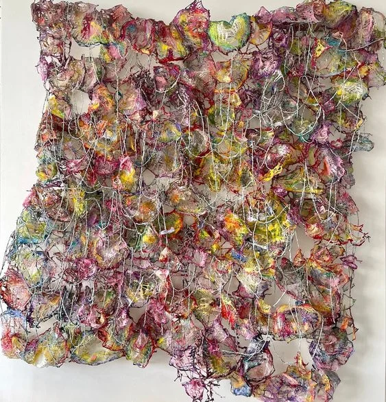 Abstract mixed media artwork with colorful, irregular, crumpled paper and string arranged in a dense, chaotic pattern on a white background.