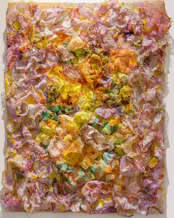 Abstract textured artwork with crumpled, multicolored paper or fabric in pink, yellow, orange, and green tones.