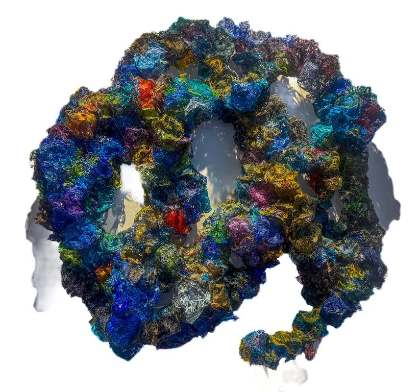 Colorful textured abstract sculpture with circular and spiral shapes, composed of multicolored material, casting a shadow on a white background.