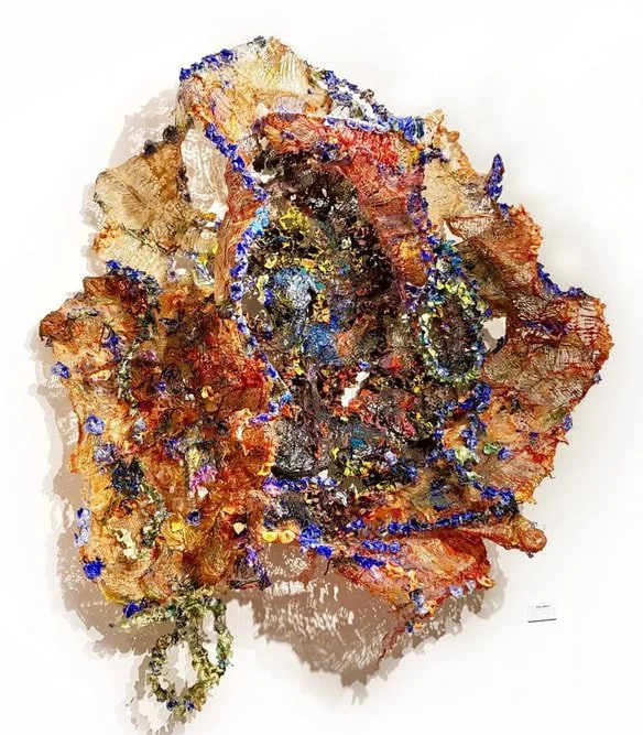 Mixed media abstract artwork resembling a flower with textured layers of brown, orange, blue, and gold colors.