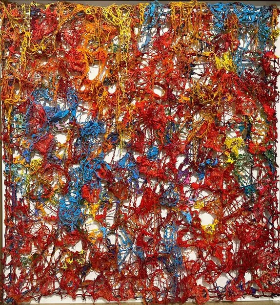 Abstract mixed-media artwork with tangled red, yellow, blue, green, and orange threads or strings on a white background.