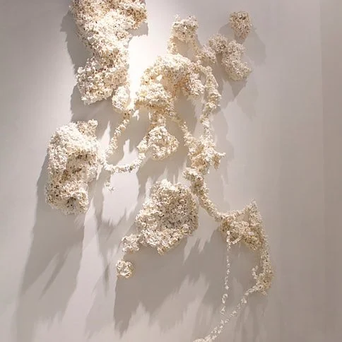 Abstract wall sculpture made of white textured materials on a gray wall.