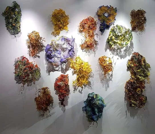 Colorful abstract sculptures arranged on a white gallery wall.