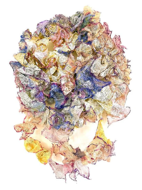 A colorful, abstract artwork resembling a face created with crumpled, layered fabric or paper in various pastel and vibrant hues against a white background.