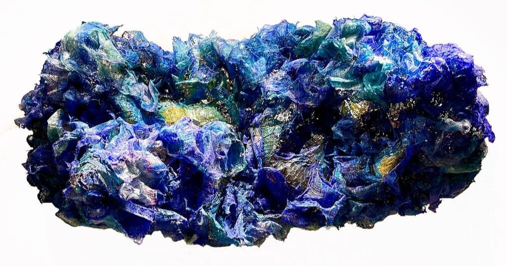 Close-up of a crumpled, multicolored, iridescent fabric with shades of blue, purple, green, and gold.