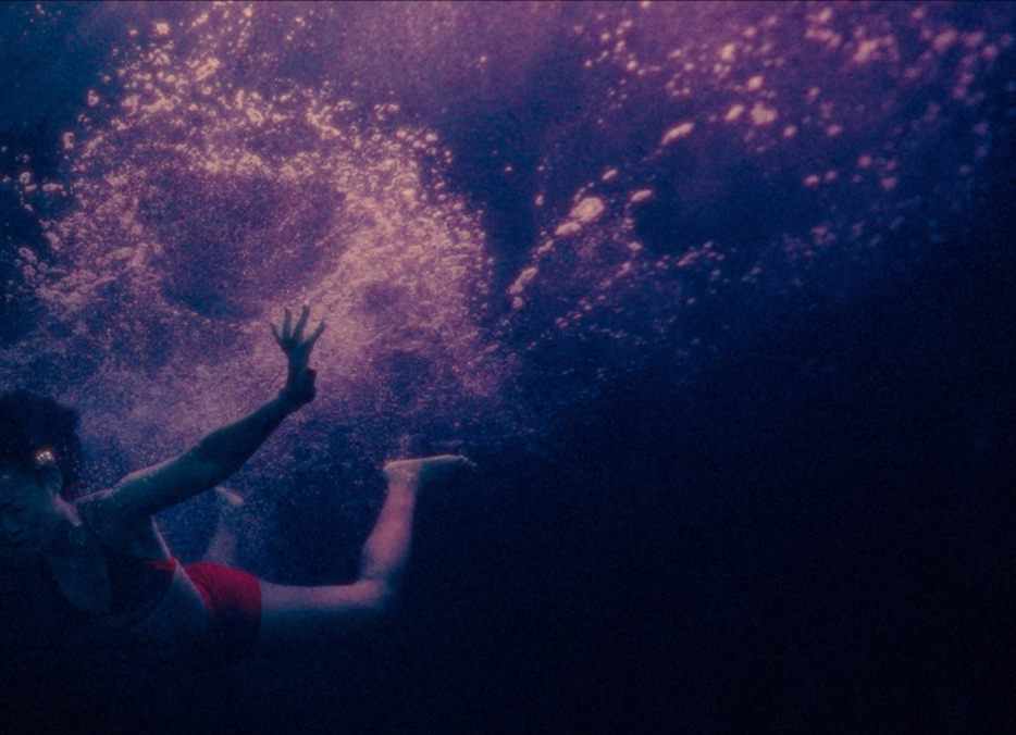 Elle underwater bathed in deep blues and purples from the short film Betta Fish