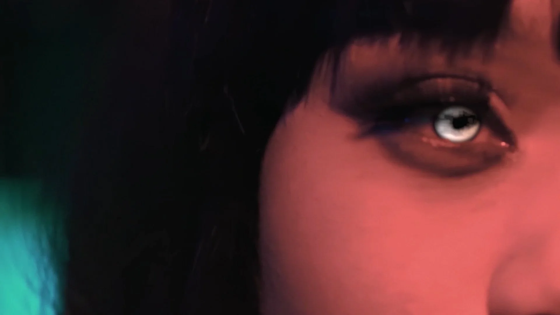 Close-up of a person's eye with makeup, with black hair and colorful lighting.