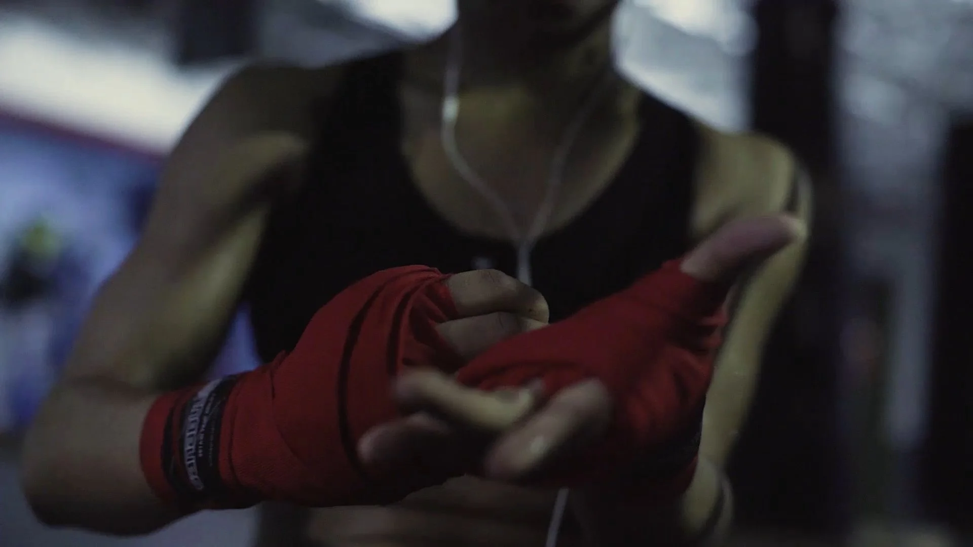 A person wearing black and yellow athletic clothing, red gloves, and white earphones, forming a heart shape with their hands.