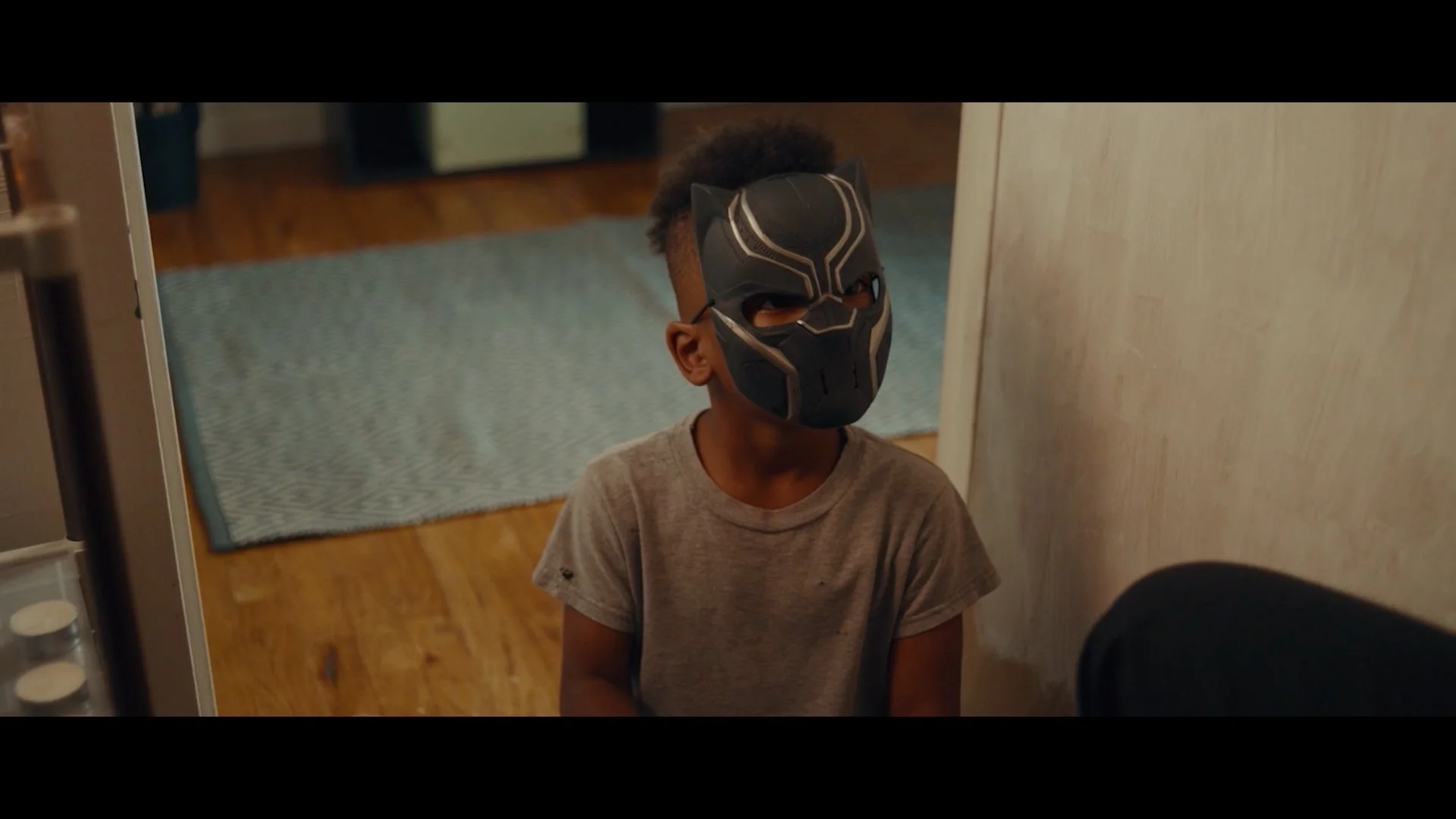 A young boy wearing a Black Panther mask standing inside a house.