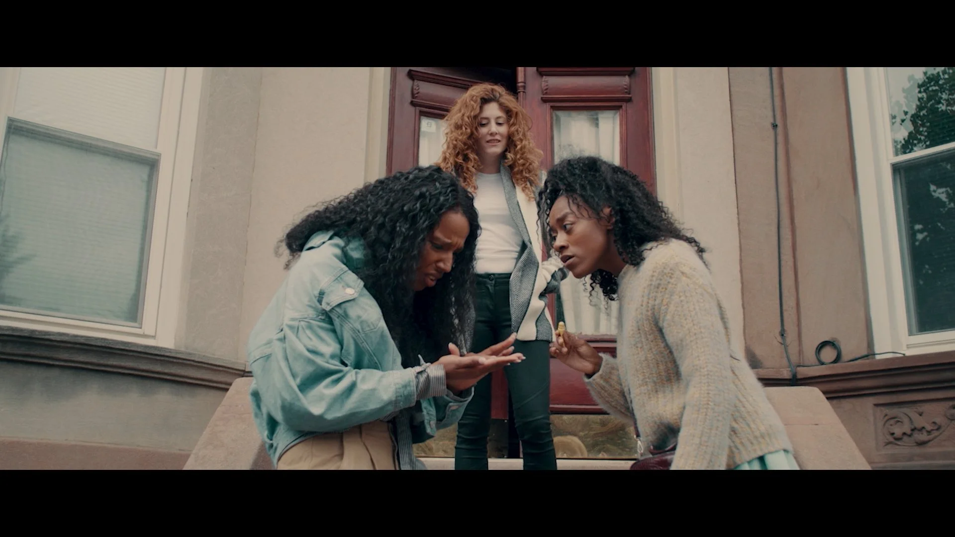 Three women standing outside a house, looking at something in her hand.