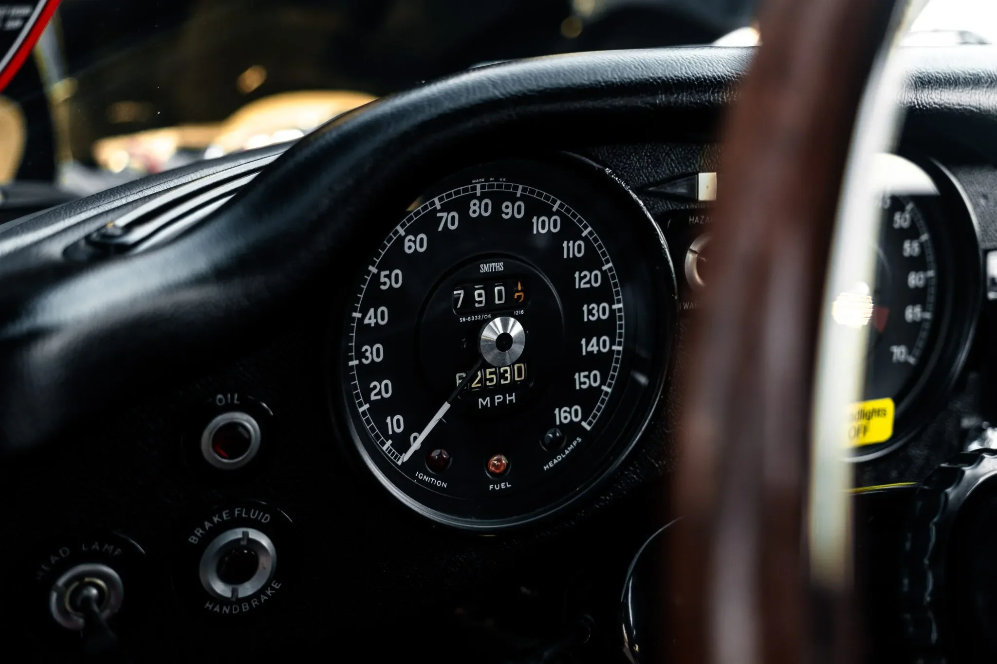 Close-up of a Jaguar E-Type XKE speedometer and dashboard. The interior includes various gauges and controls.
