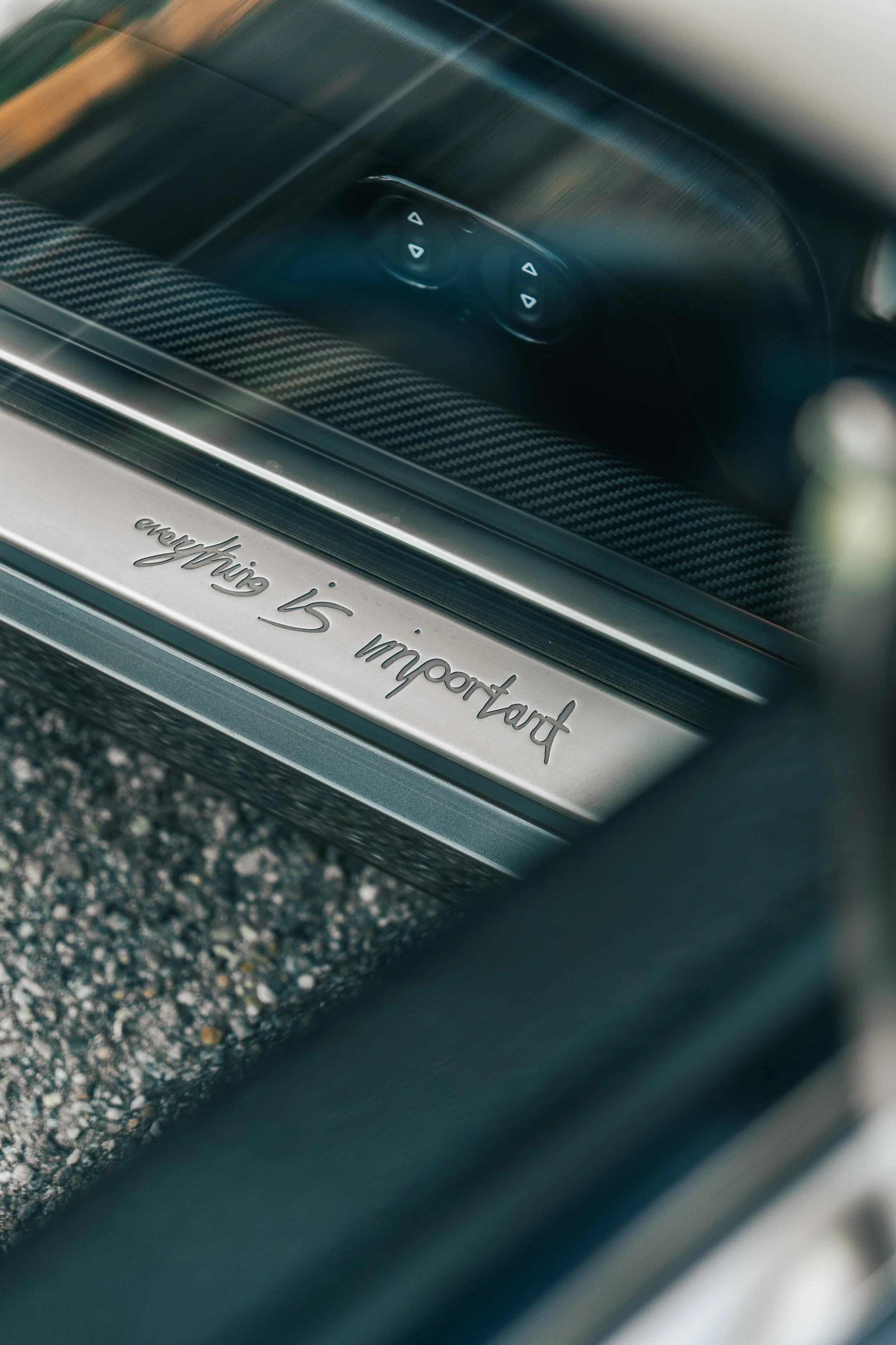 Close-up of a Singer Porsche 911 door sill plate with the engraved message 'everything is important' and a set of window control buttons on the seat in the background.