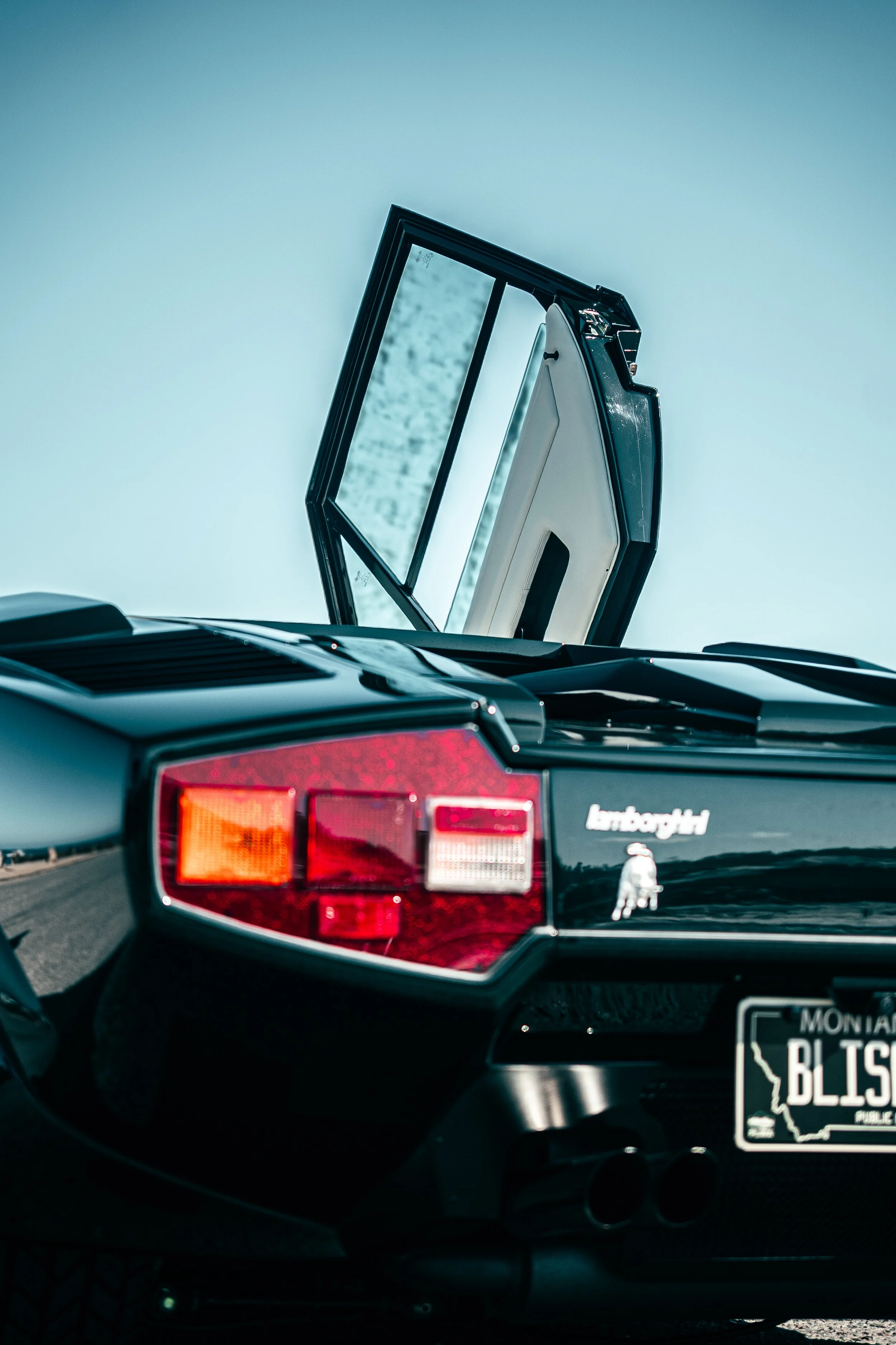 The rear of a Lamborghini Countach with its door open, showing part of the interior. Blue sky in the background.