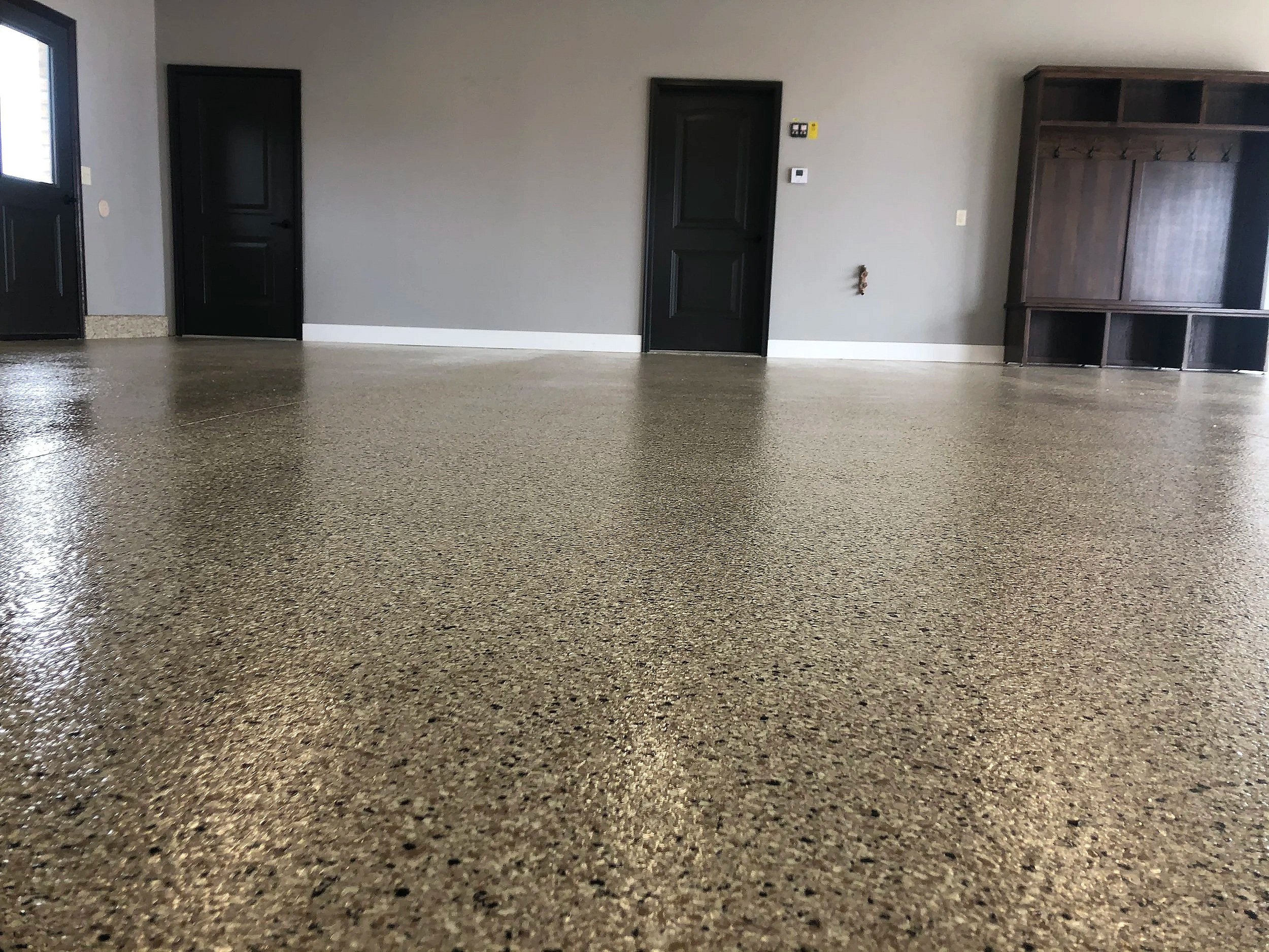 Photo of an empty room with gray walls, black doors, a dark brown wooden cabinet, and polished concrete flooring.