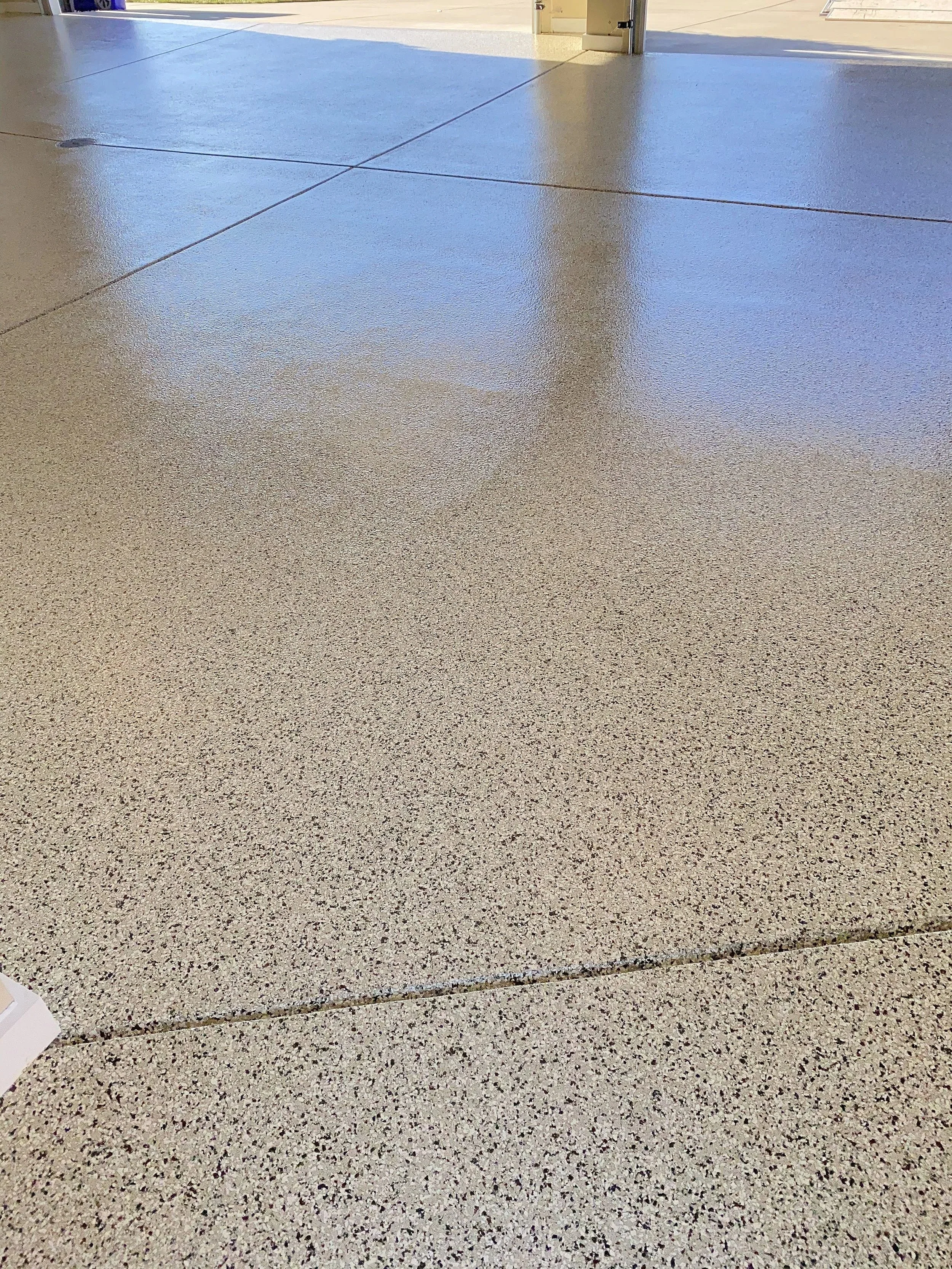 Polished concrete or epoxy floor in an open garage or utility room with bright natural light.