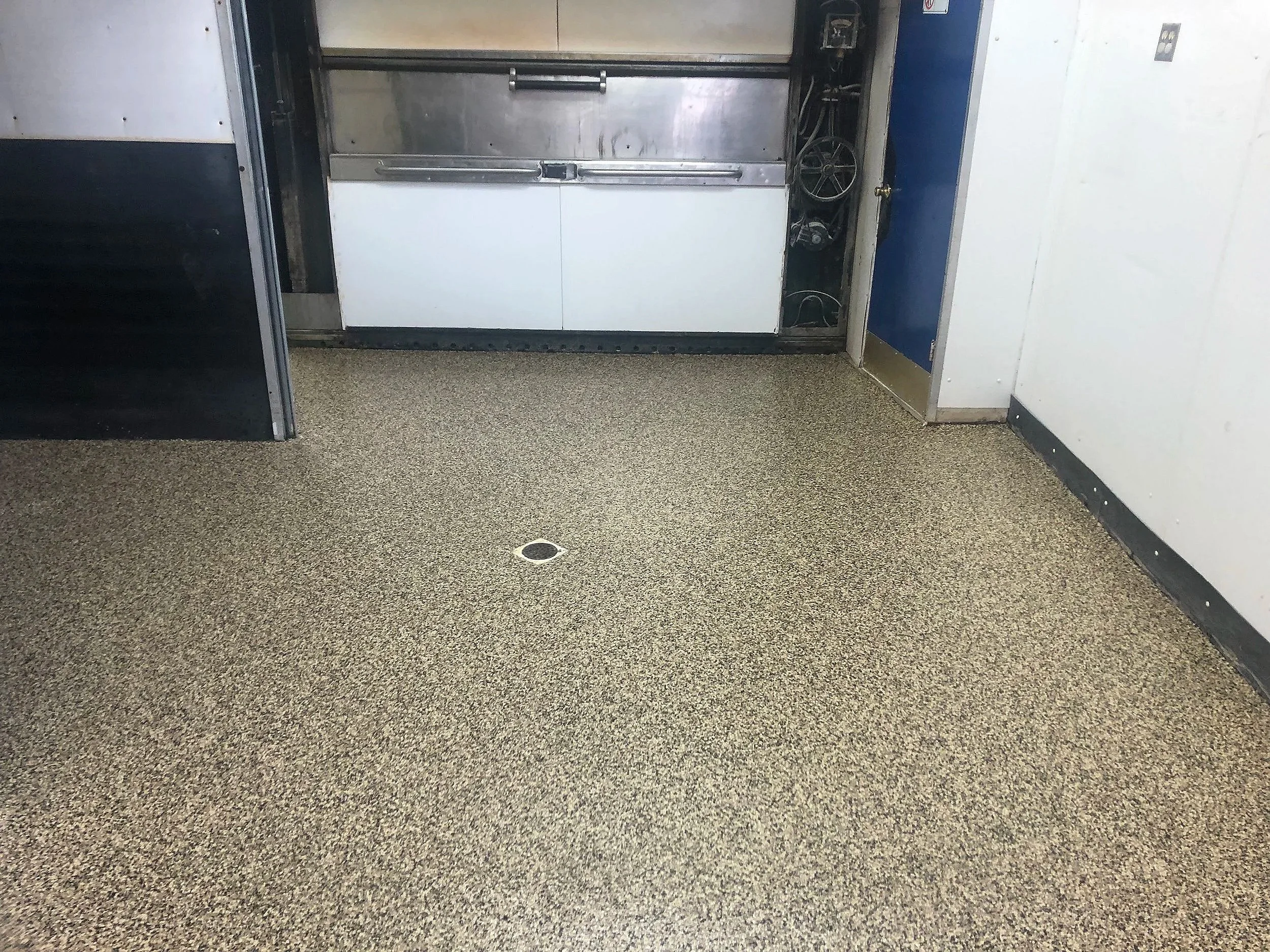 Empty room with commercial flooring, a drain in the center of the floor, and a metal door with a handle.