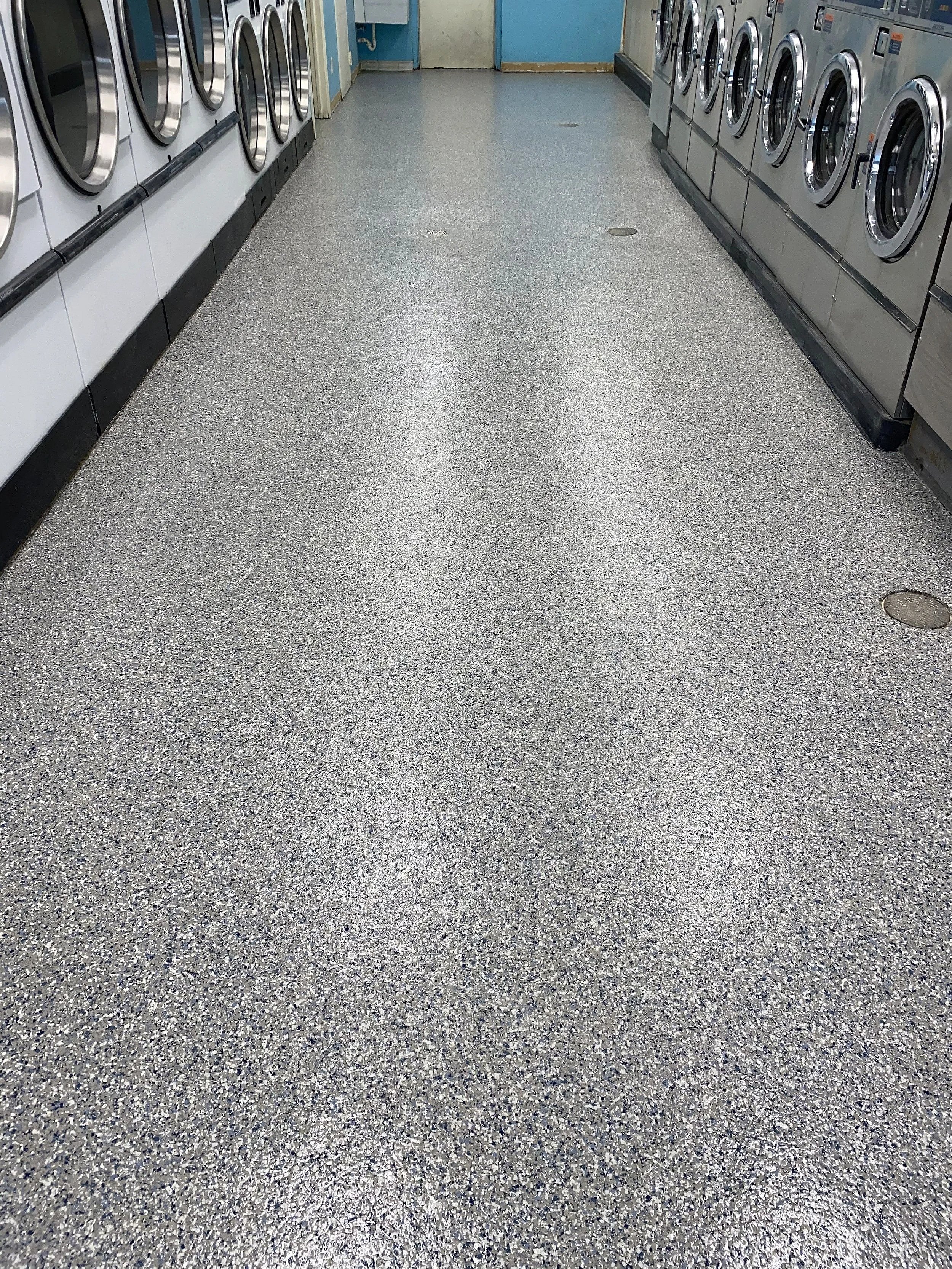 Laundry room with a speckled gray floor, washing machines on both sides, and a door at the back.
