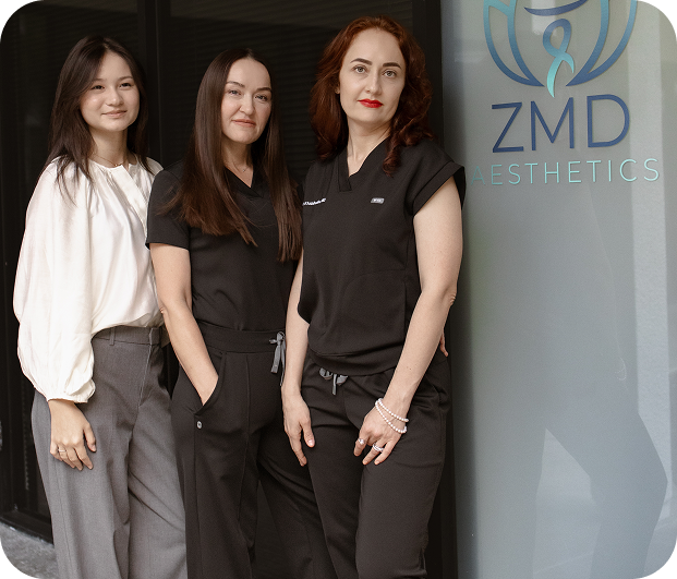 Three women standing in front of ZMD Aesthetics sign outside a building, smiling at the camera.