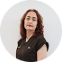 A woman with curly hair wearing a black top, standing against a plain white background.
