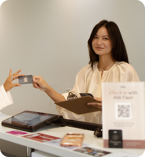 A woman smiling at a reception desk, handing over a card to another person.