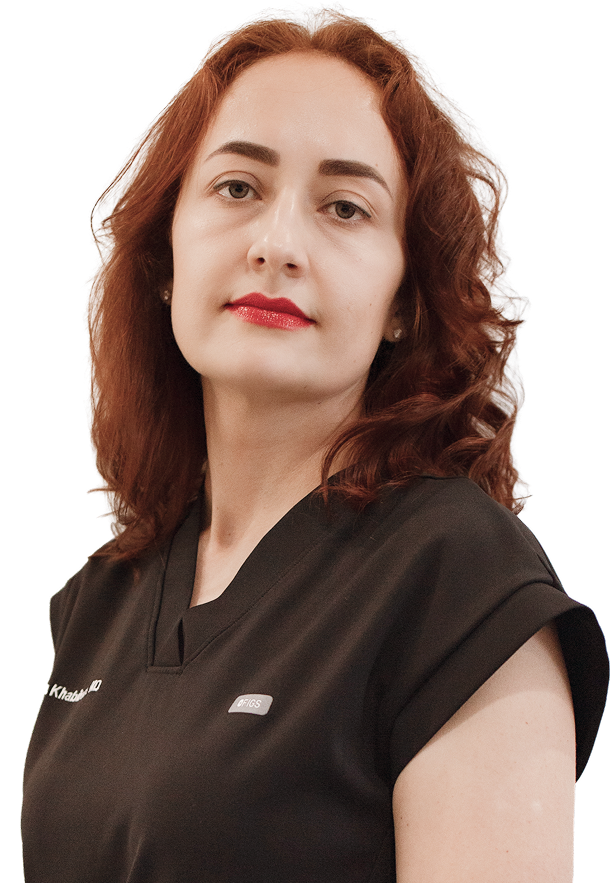 A woman with curly red hair, fair skin, and red lipstick, wearing a black top, looking at the camera.