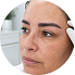 Close-up of a woman with makeup being applied to her eyebrows by a makeup artist