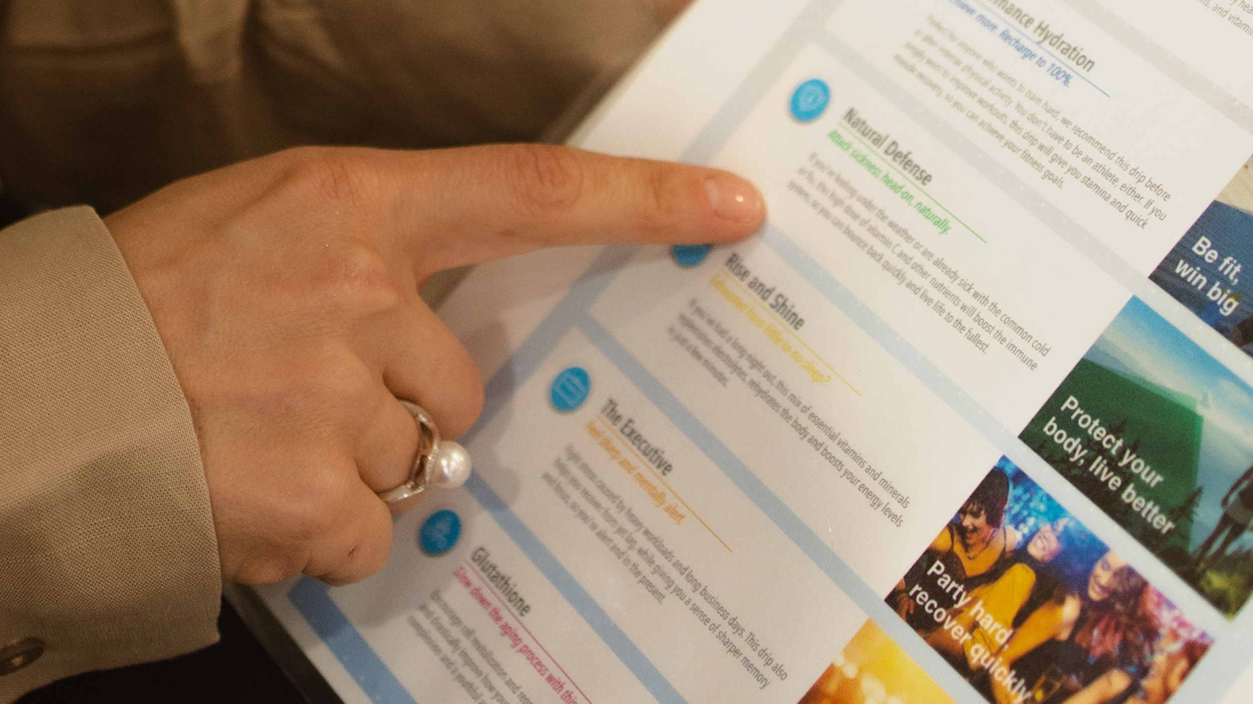 Close-up of a person's hand holding and pointing at a colorful health and wellness newsletter or brochure with text and images about hydration, immune health, and fitness.