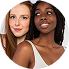Two women with curly hair standing close together, one with dark skin and the other with light skin, both smiling.
