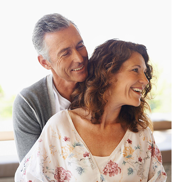 A happy older man and woman smiling and looking at each other indoors.