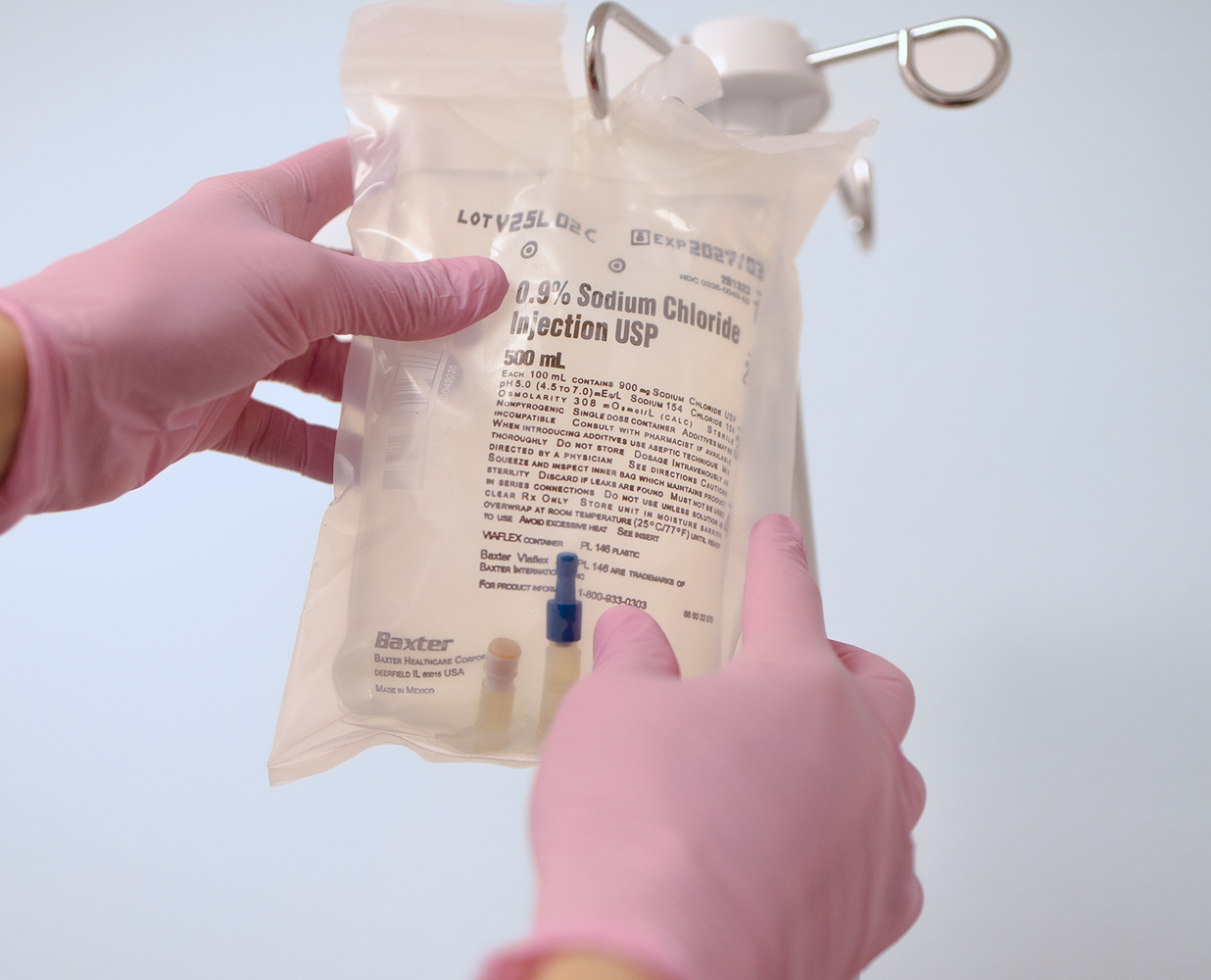 A healthcare professional wearing pink gloves holding a bag of sodium chloride injection with a needle inserted, used for medical purposes.