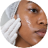 Close-up of a woman with clear skin and makeup, holding a cotton pad to her face