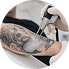 Close-up of a person's arm with tattoos being tattooed by a tattoo artist using a tattoo machine.