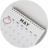 Close-up of a paper calendar with a pink marker circle around a date, resting on a white surface