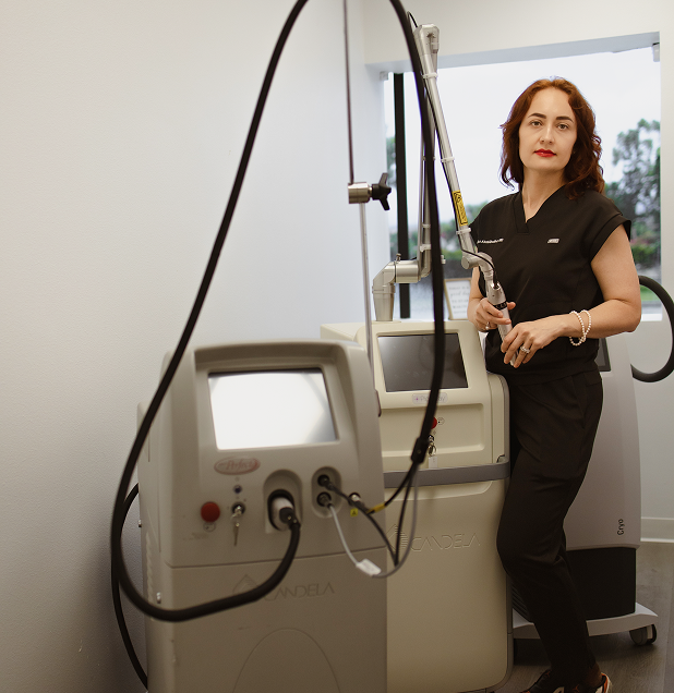 A woman standing next to medical equipment in a clinical setting, holding a handheld device.