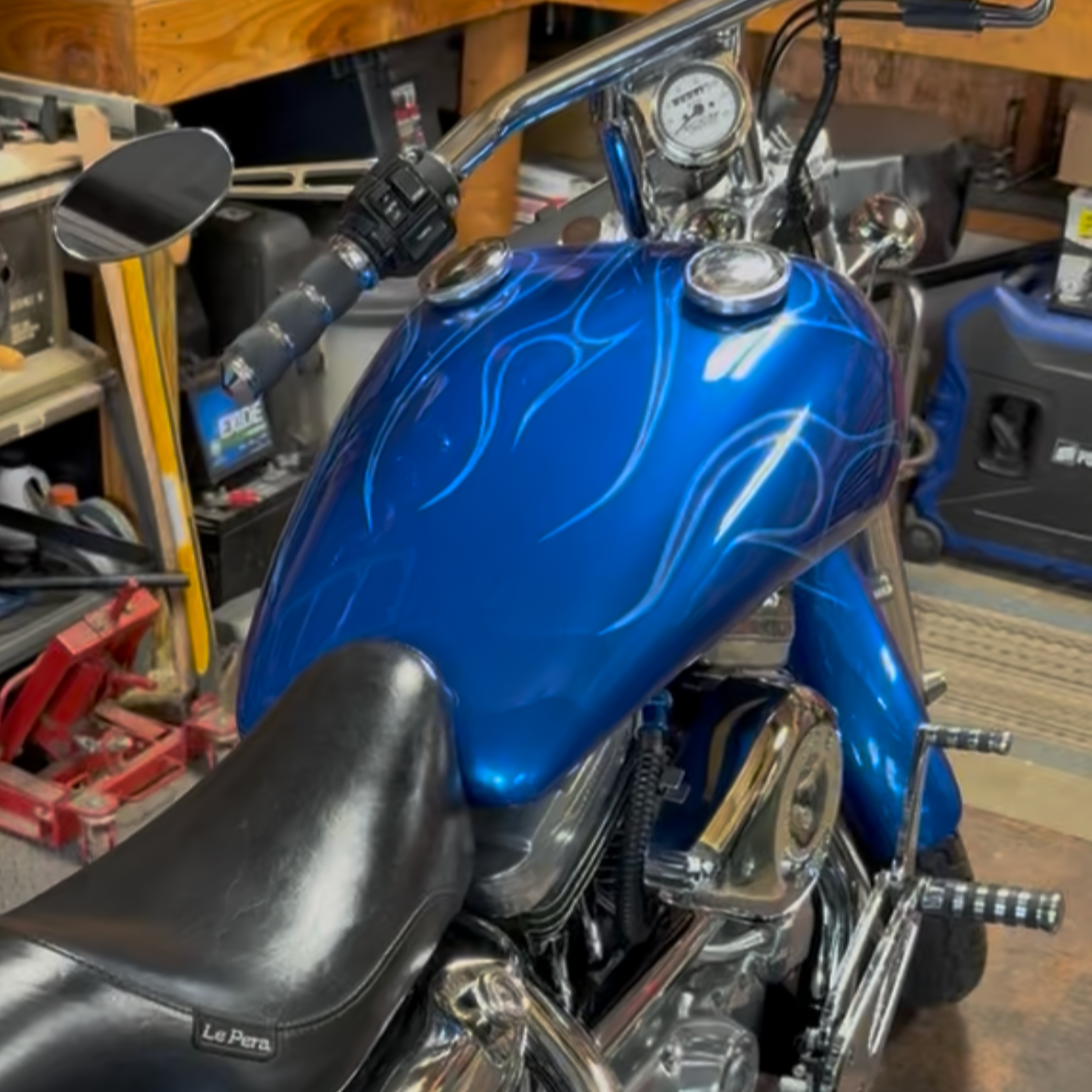 A blue motorcycle with flames painted on the gas tank, parked in a garage with tools and equipment around.