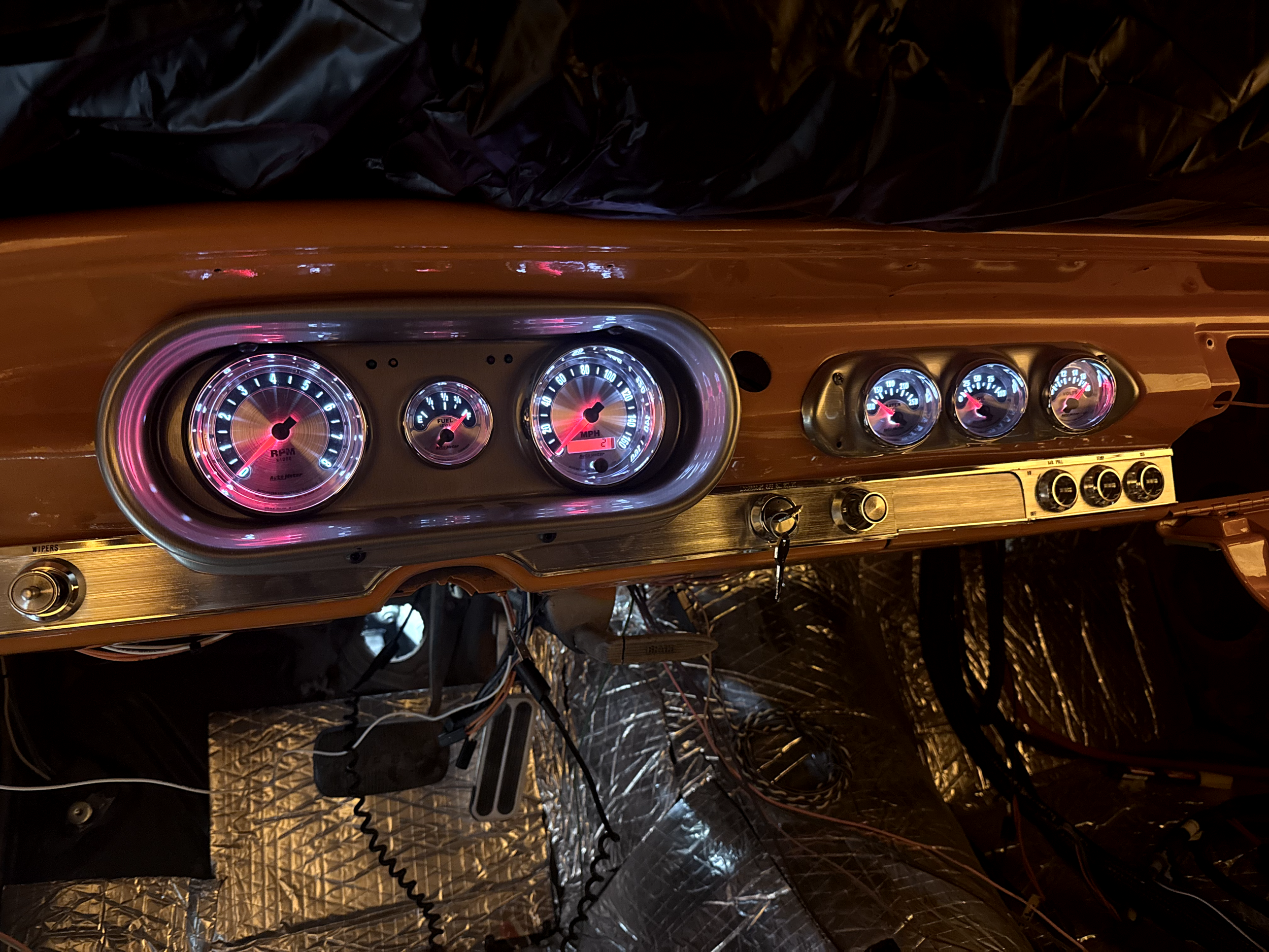 A car dashboard showing speed, RPM, fuel, and temperature gauges, with various wires and electronic components visible underneath.