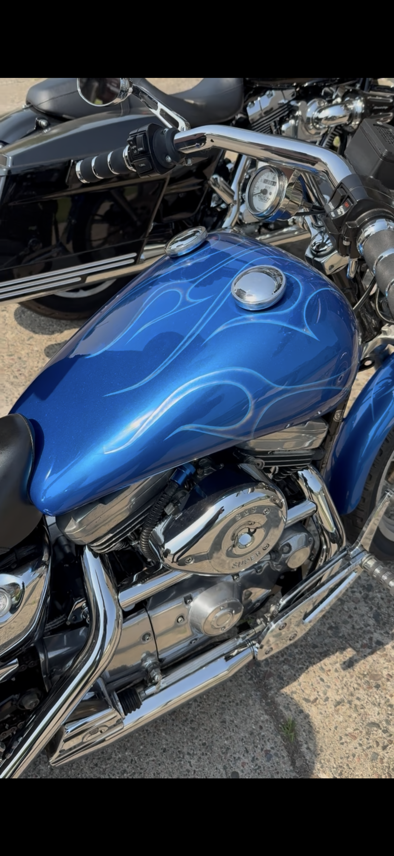 Close-up of a blue motorcycle with white flame decals, chrome engine parts, and black seat, parked outdoors.