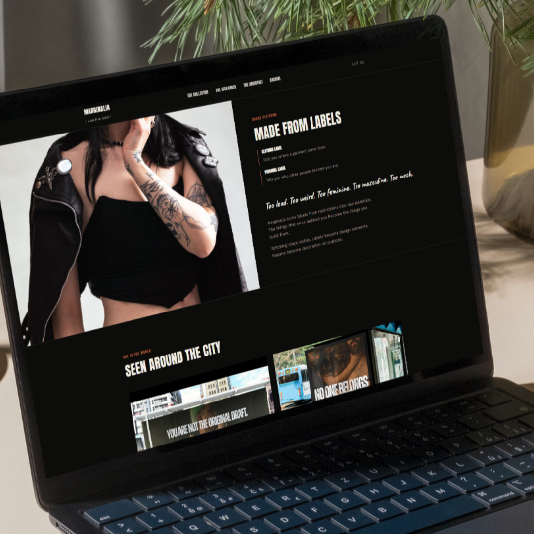 Laptop screen displaying a website with a large photo of a tattooed woman in a black leather jacket, with text about branding and labels. The website has a dark theme with white and orange text.