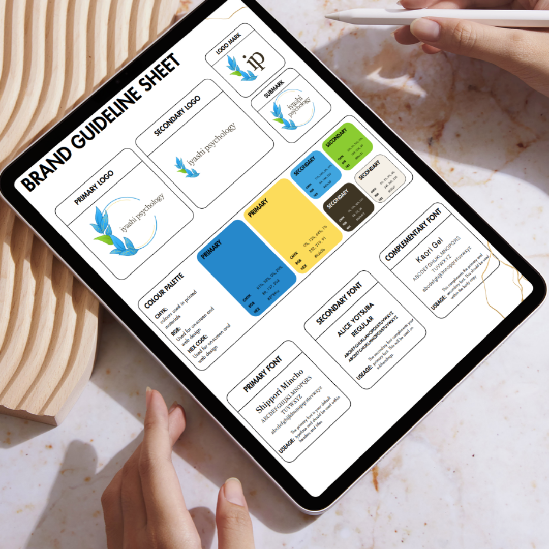 Digital tablet displaying a brand guideline sheet for Isayashi Psychology, including logos, color palette, fonts, and usage instructions, resting on a marble surface with a person's hand holding a stylus.