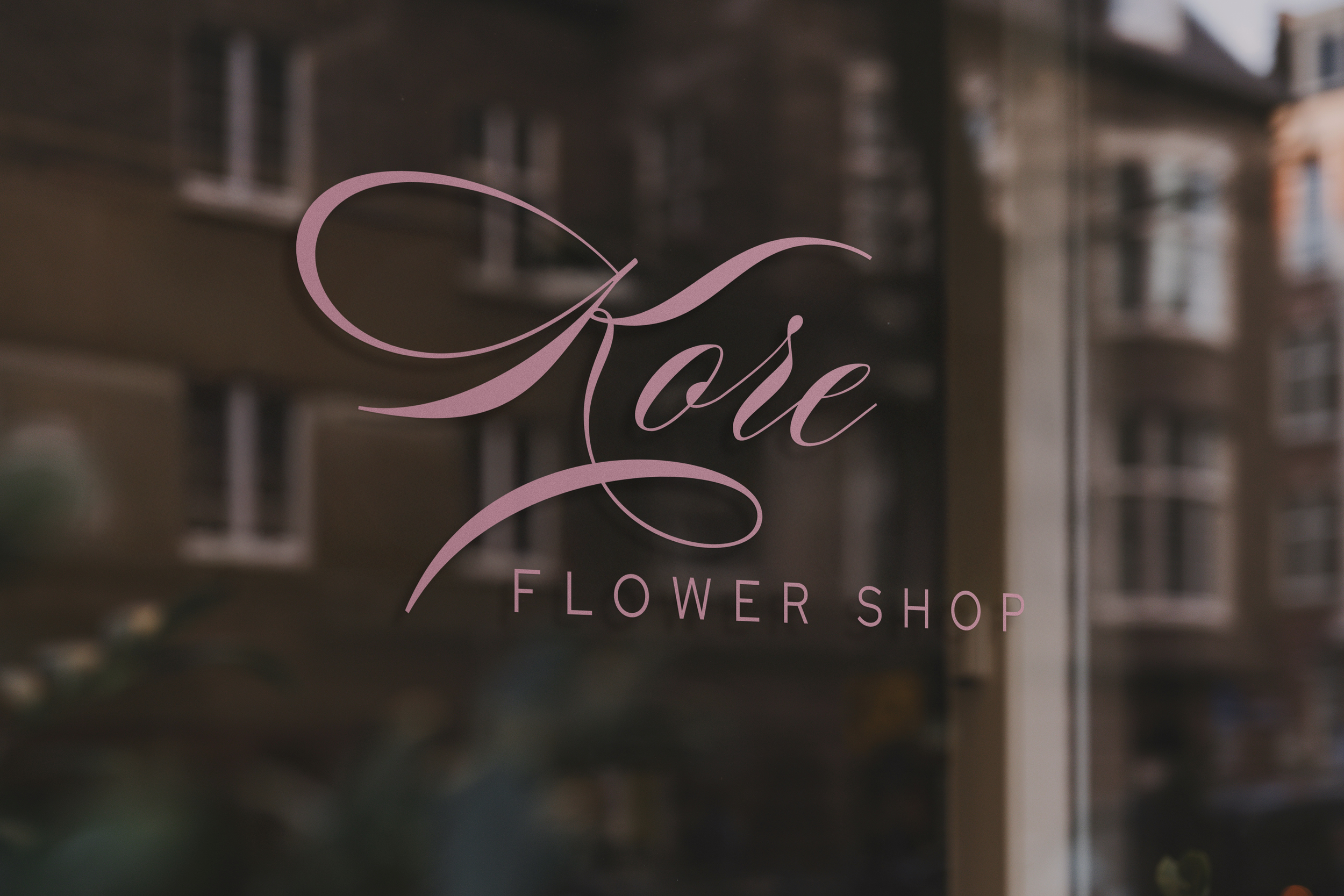 Close-up of a glass sign for a flower shop with elegant pink cursive lettering, reflected on a building window.