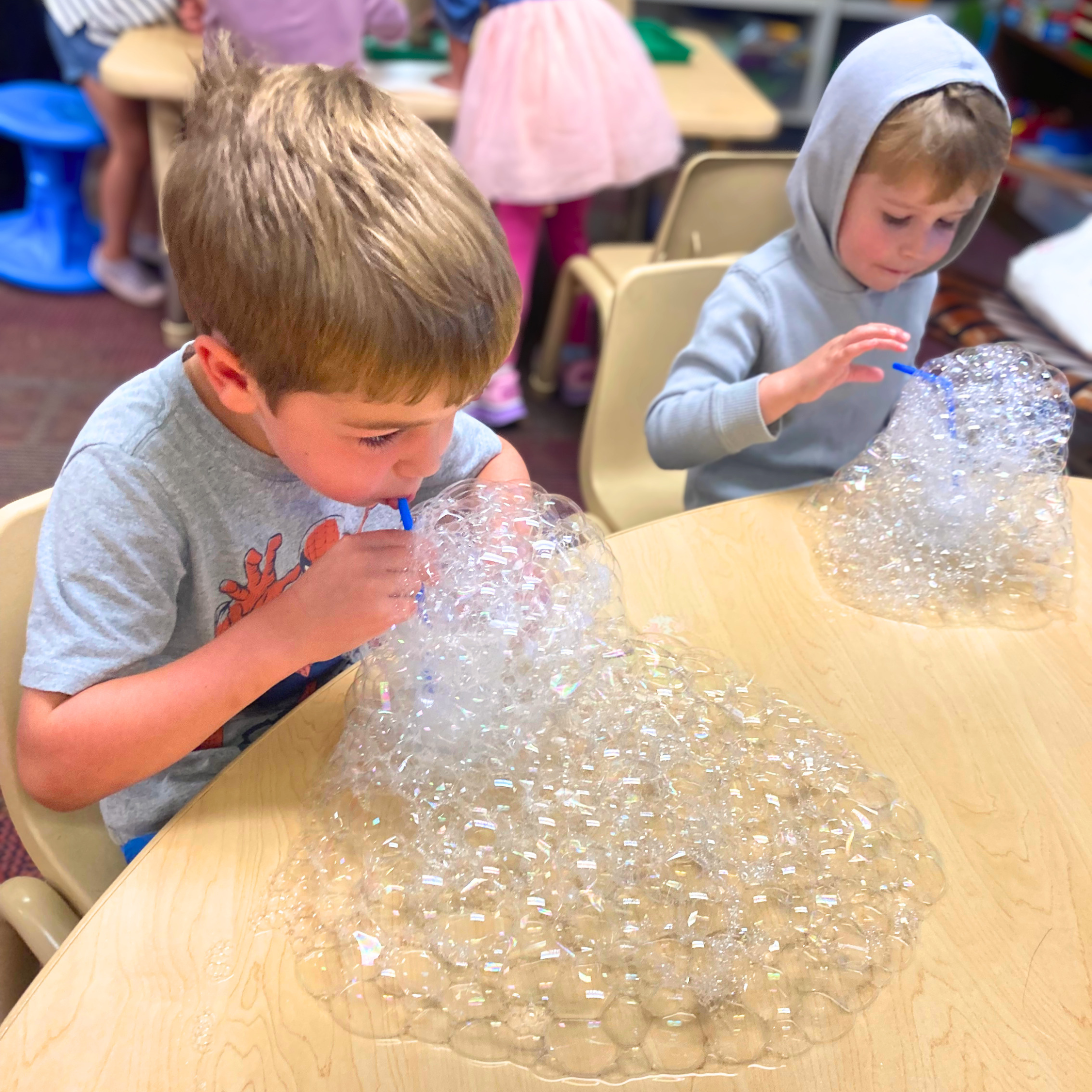 Children at a table playing with bubble solution and blowing bubbles.