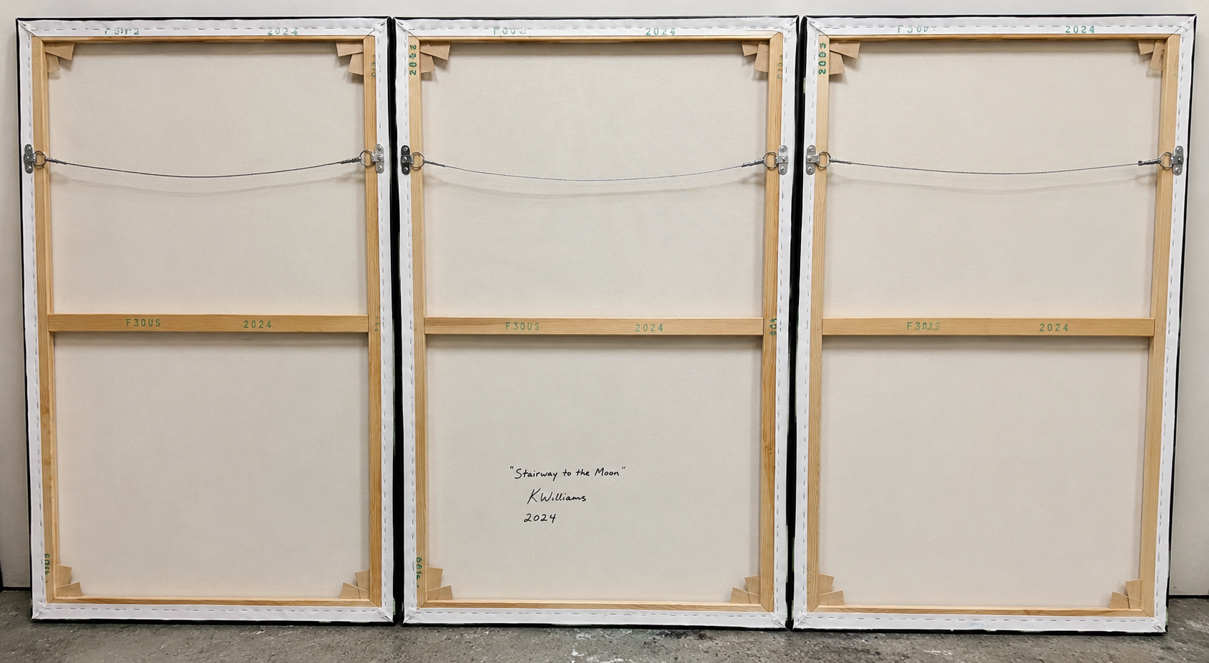 The back of three large canvases with wooden frames, labeled with the title 'Stairway to the Moon' by K. Williams, dated 2024.