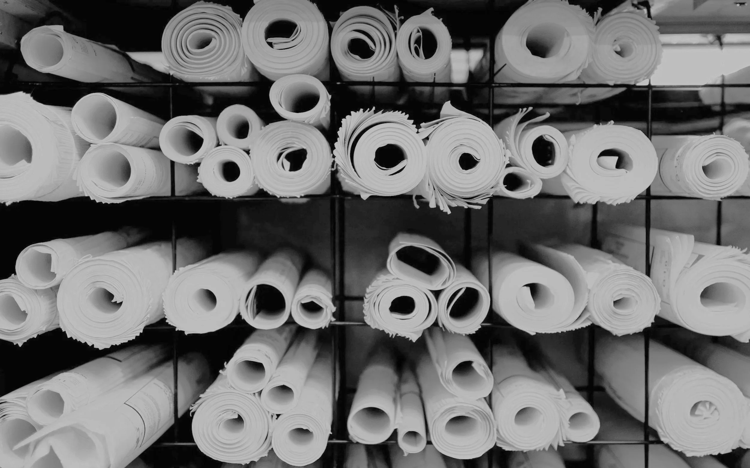 Black and white image of shelves filled with rolled-up papers or blueprints organized in rows.