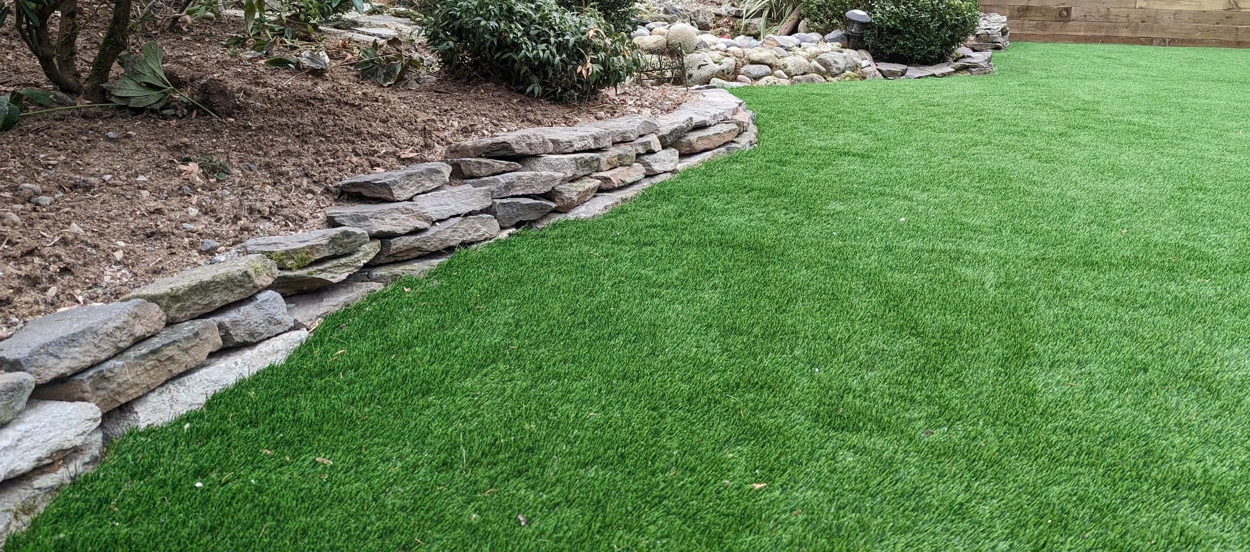 Artificial turf with a natural stone, basalt wall - Burnaby backyard