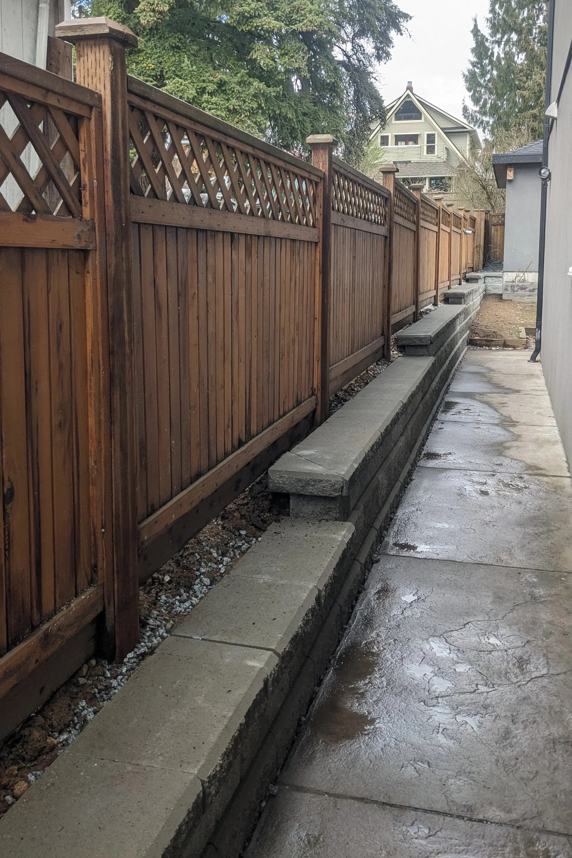 Newly installed Allan Block retaining wall with wooden fencing behind - New Westminster backyard