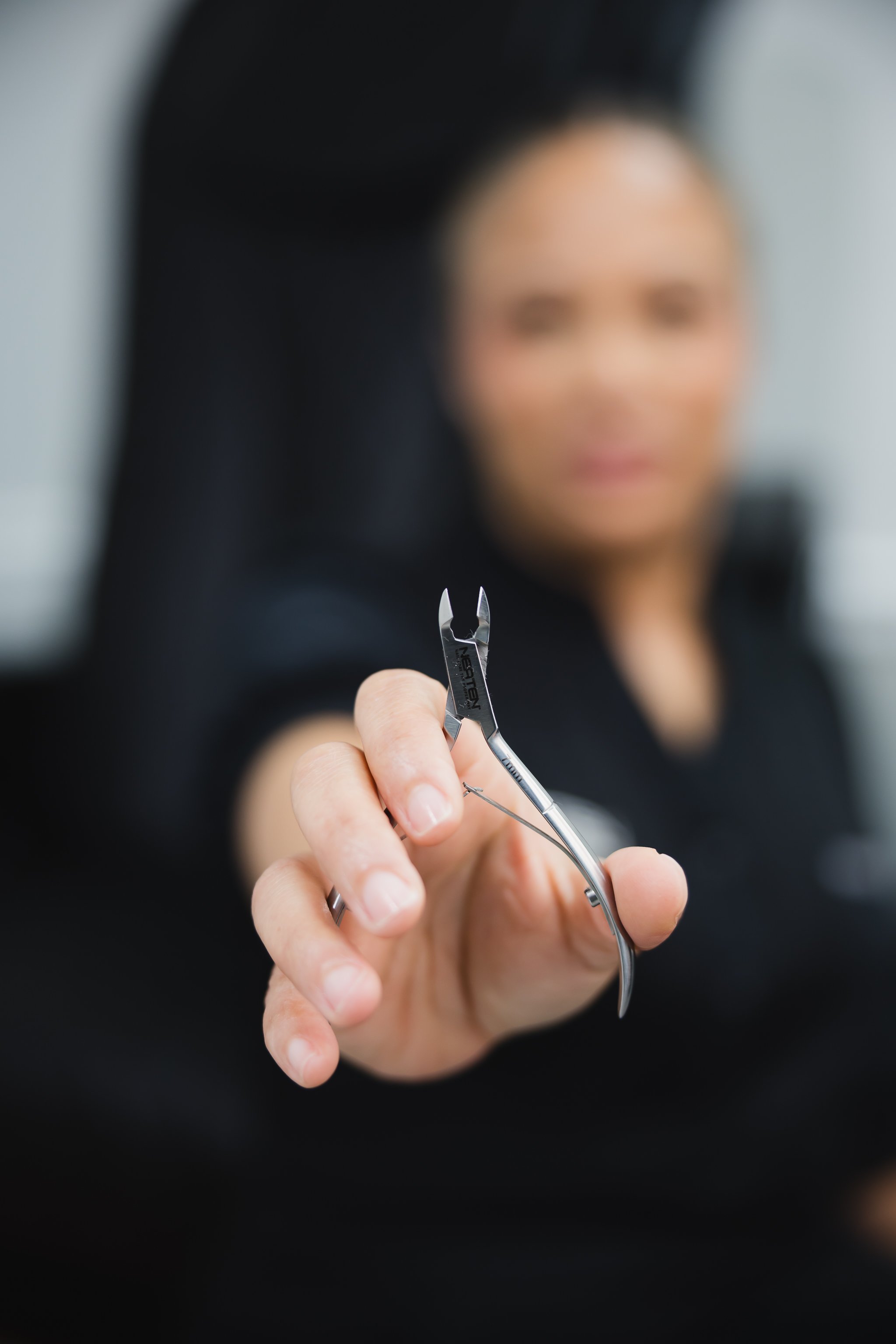 Close-up of a woman holding eyelash extension tweezers, with her face blurred in the background.
